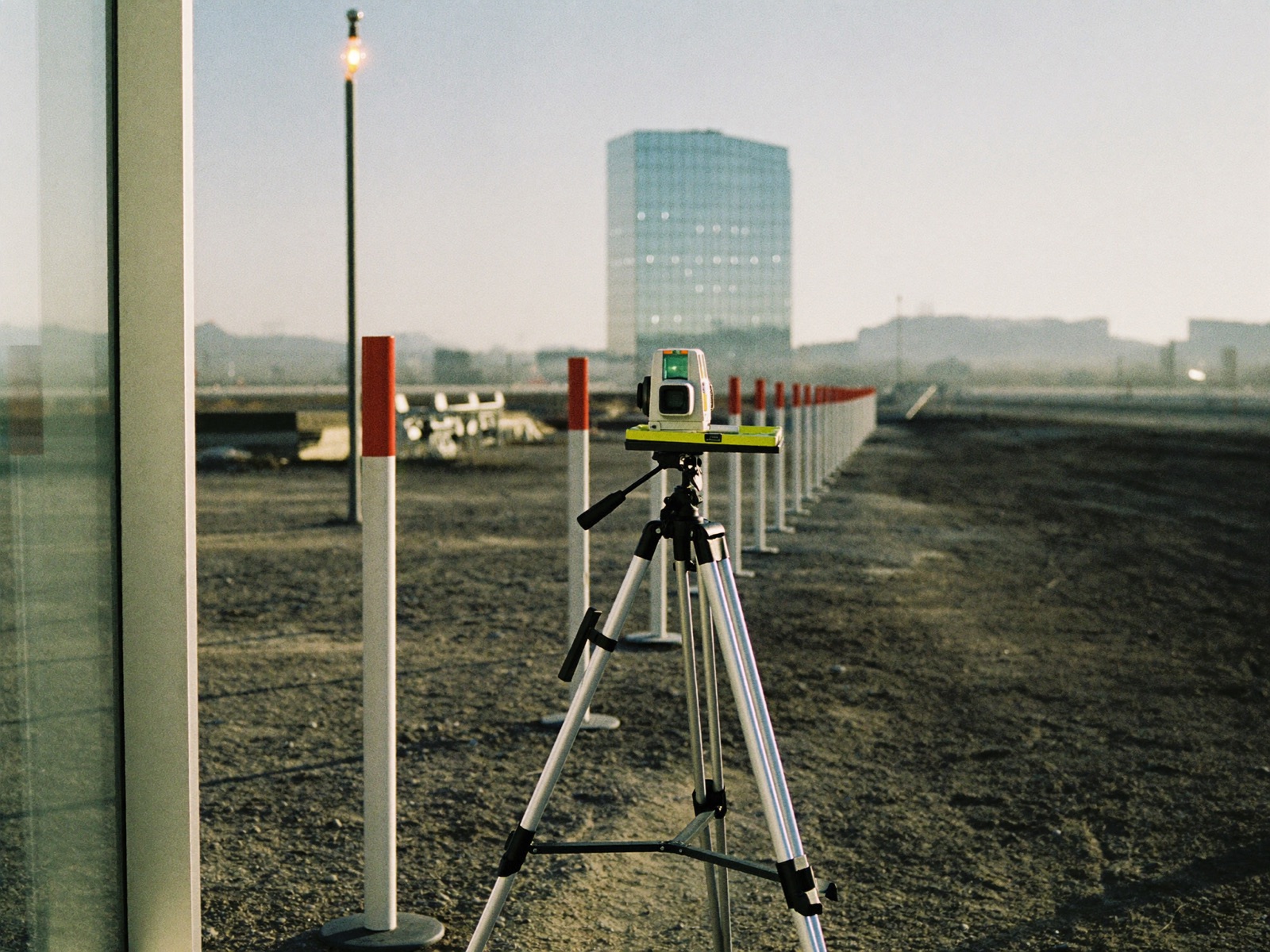 Terreno de obra al amanecer con un tripié de topógrafo y estacas antes de construir